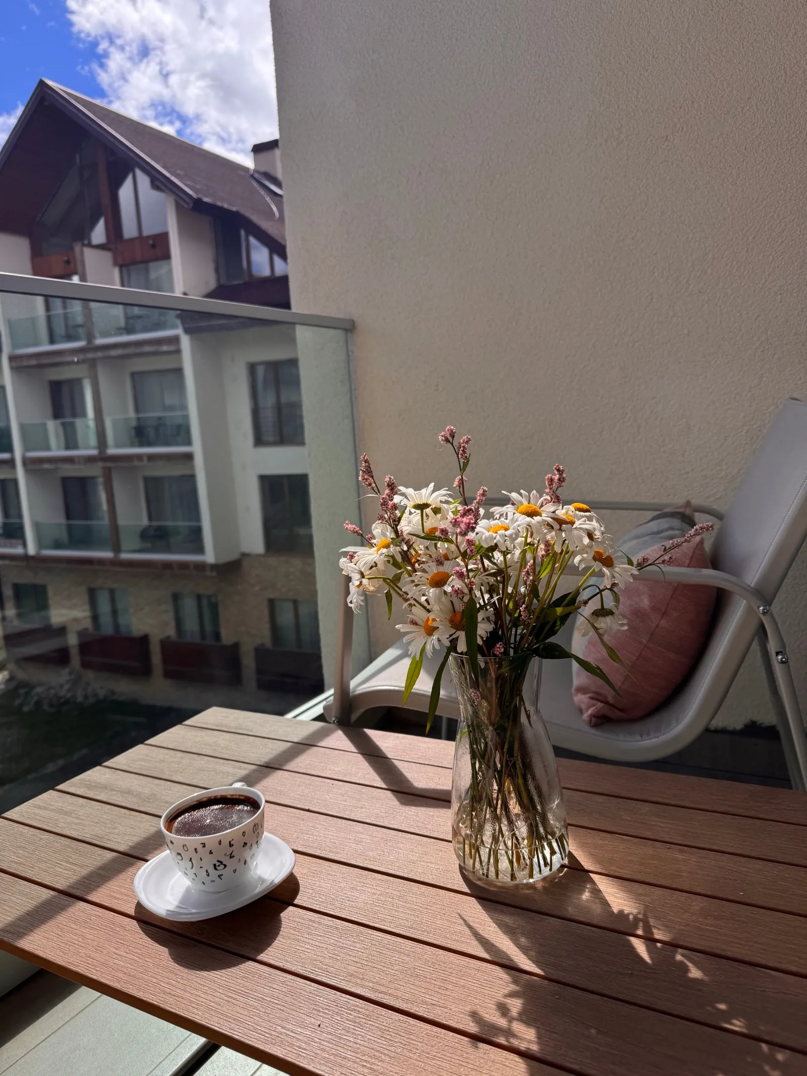 Coffee and a jug of daisies on the balcony table, on a clear morning